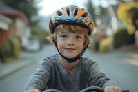Young child wearing protective cycling helmet smiling while riding bike on suburban street, natural lighting and shallow depth of field create warm atmosphere.