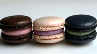 Three colorful French macarons in row on white background. Chocolate brown, pink and black sandwich cookies with cream filling isolated for bakery design.