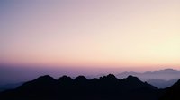 Mountain silhouettes at dawn with purple pink gradient sky and layered peaks creating peaceful atmospheric landscape for meditation and nature themes.