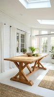 Bright sunlit dining room with wooden trestle table, white brick walls, skylights, and potted plants. Modern farmhouse interior design with natural light and contemporary furnishings.