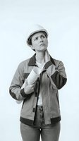Female construction worker, Caucasian ethnicity, wearing white hard hat and work jacket, holding rolled blueprints, looking upward thoughtfully against white background. Suitable for construction, engineering, architecture, and professional industry concepts.
