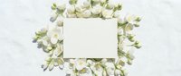 Blank white card surrounded by fresh white and green flowers on marble background, flat lay composition for wedding, greeting, or stationery design.