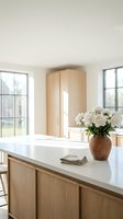 Modern minimalist kitchen interior with light wood cabinets, white countertop, fresh flowers in ceramic vase and natural lighting from large windows.
