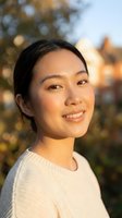 Young Asian woman smiling warmly in soft golden hour light wearing cream sweater with blurred autumn background for lifestyle and wellness content.