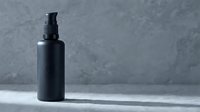 Black cosmetic pump bottle on concrete surface with minimalist styling for skincare and beauty product packaging design.