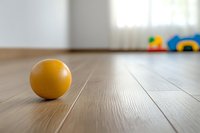 Yellow ball on wooden floor with blurred toys in background, minimalist composition with selective focus and copy space for text or design elements.