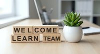 Wooden letter blocks spelling WELCOME LEARN TEAM on office desk with succulent plant and laptop creating motivational workspace for corporate training.