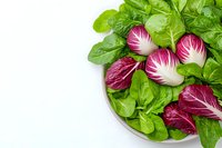 Fresh green spinach leaves and red radicchio chicory in white ceramic bowl on light background. Healthy organic salad ingredients for cooking.