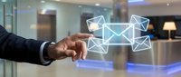 Businessman in dark suit touching digital envelope icons floating above his hand in modern office lobby, representing email communication and digital messaging technology.