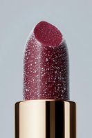 Burgundy lipstick covered in water droplets against gray background, macro photography showing texture detail and gold metallic holder for cosmetic advertising.