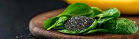 Fresh green spinach leaves with black chia seeds on wooden cutting board against dark background, healthy superfood ingredients panoramic shot.
