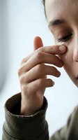 Young woman gently touching face with hand in soft natural light showing skincare routine and self-care moment with closed eyes and peaceful expression.