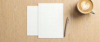 Blank white paper sheets with pen and coffee cup on wooden desk surface for business correspondence and creative writing projects.