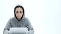 Young Caucasian woman in gray hoodie working on laptop computer at white desk, focused expression, remote work setup for business presentations.