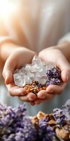 Female hands holding clear quartz crystals, dried lavender flowers and walnuts in cupped palms against soft natural lighting, creating spiritual wellness atmosphere.