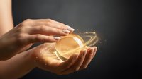 Young woman with medium skin tone holding glowing golden orb with magical light particles, symbolizing energy, wellness, and spiritual power for healing and transformation concepts.