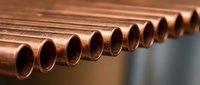 Row of shiny copper pipes arranged in perfect alignment for industrial plumbing and construction applications in manufacturing facilities.