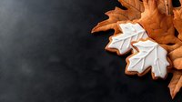 Festive maple leaf cookies with white icing glaze on dark background. Autumn themed gingerbread biscuits with detailed frosting decoration for seasonal baking.