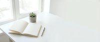 Minimalist white desk workspace with open notebook, pen and small potted succulent plant by window. Clean modern office setup for productivity and focus.
