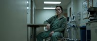 Female healthcare worker in green scrubs sitting in hospital corridor during break time reflecting on medical profession and patient care responsibilities.