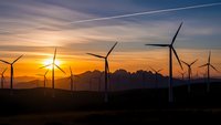 Wind turbines generating renewable energy at sunset with mountain silhouettes and dramatic sky creating sustainable power landscape for environmental projects.