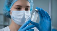 Female healthcare worker in protective gear examining medical vial in laboratory setting for pharmaceutical research and vaccine development.