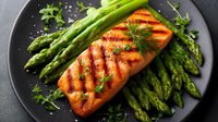 Grilled salmon fillet with fresh asparagus spears and herbs on dark plate. Healthy protein and vegetable meal for restaurant menu or cooking blog.