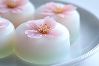 Delicate pink cherry blossom wagashi on white plate, traditional Japanese confectionery with soft pastel colors and floral design, sweet mochi dessert.