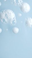 White soap bubbles and foam floating on light blue background, ideal for skincare, cosmetics, and wellness product marketing.