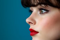 Side profile portrait showcasing bright red lipstick, dramatic eye makeup, and straight dark bangs against turquoise background. Professional beauty and cosmetics concept.