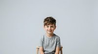 Young boy with brown hair and fair complexion wearing gray t-shirt, smiling at camera against white background. Studio portrait suitable for family, education, and lifestyle design projects.