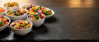 Colorful jelly beans candy in white ceramic bowls arranged on dark wooden surface for sweet treats and confectionery displays.