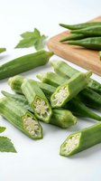 Fresh green okra pods sliced and whole on white background with wooden cutting board showing seeds inside for healthy cooking and nutrition.