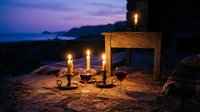 Romantic candlelit dinner setup on beach at twilight with wine glasses, wooden table, and ocean view creating intimate atmosphere for couples celebration.