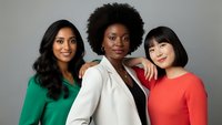 Three diverse professional women standing together in colorful business attire, representing teamwork and workplace diversity in corporate environment.