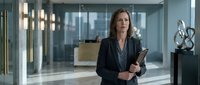Professional businesswoman in dark suit holding tablet in modern corporate office lobby with glass walls and contemporary lighting for business presentations.