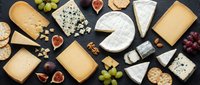 Gourmet cheese platter with variety of artisanal cheeses, fresh grapes, figs, nuts and crackers arranged on dark slate background for culinary presentations.