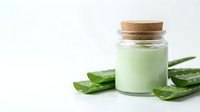 Natural aloe vera gel in glass jar with cork lid and fresh green leaves on white background for skincare and cosmetic applications.