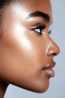Close-up profile portrait of African American woman with glowing skin, long eyelashes, and glossy lips against light background, showcasing natural beauty.