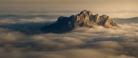 Majestic mountain peaks emerging through dramatic cloud cover during golden hour sunrise creating ethereal alpine landscape with warm atmospheric lighting.