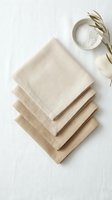 Stacked natural linen napkins in neutral tones arranged with dried wheat and sea salt bowl on white background for home decor and tableware styling.