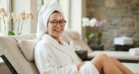 Happy Asian woman in white bathrobe and towel relaxing at luxury spa resort, smiling while enjoying wellness treatment and self-care routine.