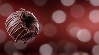 Gourmet chocolate truffle with bite mark revealing dark ganache center against blurred red bokeh background for dessert advertising.