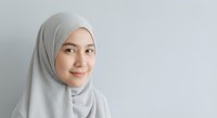 Young Southeast Asian Muslim woman in gray hijab smiling confidently against light background with copy space.