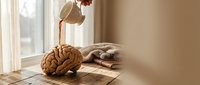 Morning coffee being poured into brain-shaped mug on wooden table with warm sunlight streaming through window creating cozy breakfast atmosphere.
