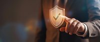 Businessman touching glowing security shield icon with checkmark representing cybersecurity protection and data safety in digital business environment.