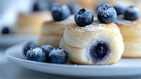 Fresh blueberry filled mini donuts dusted with powdered sugar on light ceramic plate, selective focus on front pastry with scattered berries.