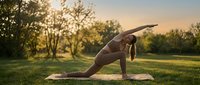 Young woman practicing yoga in peaceful park setting during golden hour sunset with warm natural lighting creating serene outdoor fitness atmosphere.