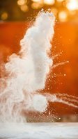 White flour explosion with powder cloud against warm orange bokeh background creating dynamic culinary motion for cooking and baking concepts.