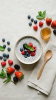 Chia seed pudding bowl topped with fresh raspberries, blueberries, and blackberries, surrounded by scattered berries and mint leaves on white linen background.